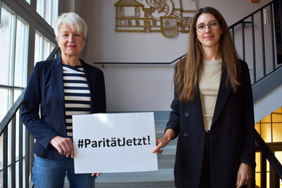 Landrätin Christiana Steinbrügge und Gleichstellungsbeauftragte Carolin Wiek halten ein Schild hoch, auf dem steht: #ParitätJetzt!