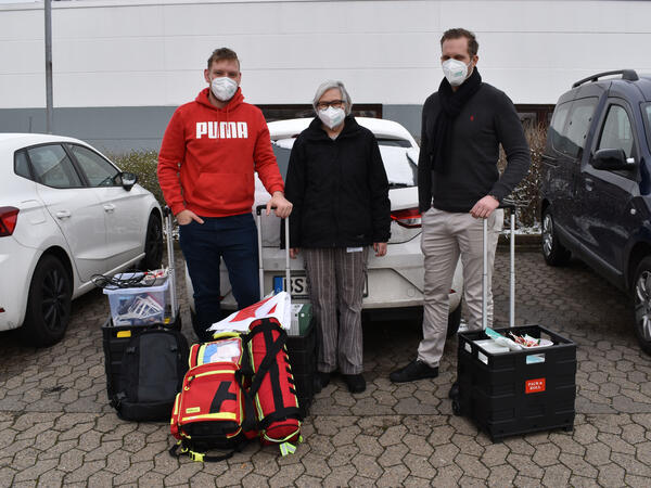 Drei Personen stehen mit Impf-Equipment vor einem Auto.
