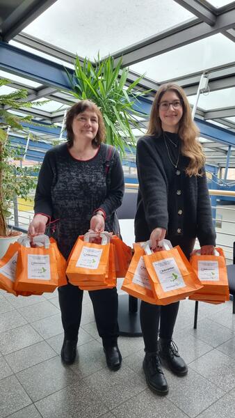 Carola Stobbe, Gleichstellungsbeauftragte des Jobcentera Wolfenbüttel und Carolin Wiek, Gleichstellungsbeauftragten des Landkreises Wolfenbüttel, halten orange Papiertüten in den Händen.