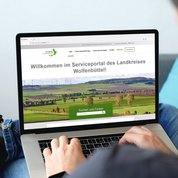Ein Laptop ist zu sehen. Zwei Hnde liegen auf der Tastatur. Auf dem Bildschirm ist eine Webseite zu sehen. Es ist das Serviceportal des Landkreises Wolfenbttel.