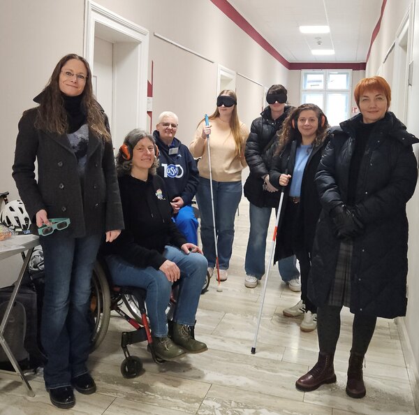 Gruppenfoto von Landkreismitarbeitenden. Sie tragen Kopfh�rer oder Augenbinden mit Blindenst�cken oder sitzen im Rollstuhl.