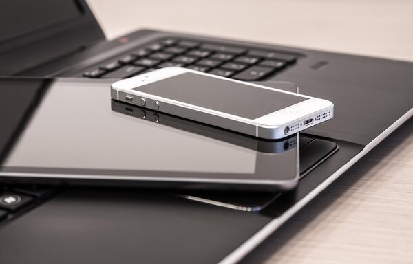Es ist ein Laptop zu sehen, auf dessen Tastatur ein Tablet und ein Smartphone liegen. 