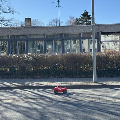 Ein rotes Bobbycar vor einem Schulgeb&auml;ude