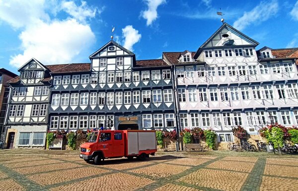 Ein Feuerwehrauto auf einem Platz. Im Hintergrund mehrere Fachwerkh�user mit roten D�chern. Blauer Himmel mit ein paar kleinen wei�en Wolken.