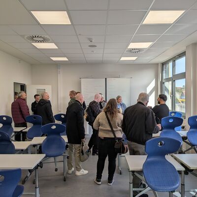 Ein Klassenraum mit mehreren Personen, die sich den Klassenraum ansehen.