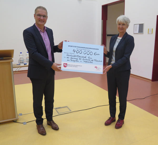 Staatssekretär Stephan Manke übergibt den symbolischen Check über 400.000 Euro an Landrätin Christiana Steinbrügge.