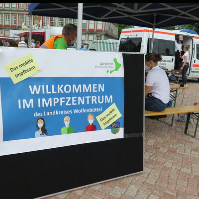 Ein Schild auf dem steht "Willkommen im Impfzentrum - das mobile Impfteam" steht auf dem Schlossplatz an einem Pavillon.